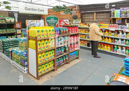 Reife Frau Gärtnerin, die Hand gehaltenen Unkrautbekämpfungsspray auf Chemikalie in den Garden Care Regalen im Gartenbau Gärtnerei-Geschäft England UK auswählt Stockfoto