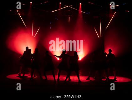 Dunkle Silhouetten tanzender Mädchen vor dem Hintergrund von Rotlicht aus Bühnenlichtern. Stockfoto