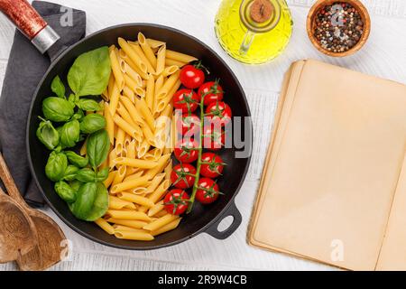 Eine lebendige Darstellung der italienischen Flagge mit Pasta, Basilikum und Tomaten, wunderschön präsentiert in einer Bratpfanne, und Kochbuchseite für Ihr Stockfoto