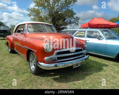 Ein altes, rotes 1951 Chevrolet Deluxe Styleline Bel Air Cabrio auf dem Rasen. Natur, Gras, Bäume. CAACMACH 2023 Oldtimer-Show. Sonniger Tag Stockfoto