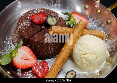 Gebackene Schokoladenfondant (Lavakuchen) mit Vanilleeis und frischen Beeren, Kupferplatte mit schwarzem Hintergrund Stockfoto