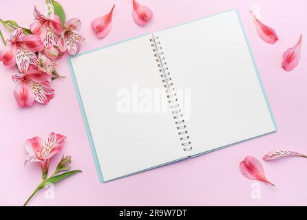 Das Notizbuch ist von rosafarbenen Alstroemeria-Blumen und -Blüten auf pinkfarbenem Hintergrund umgeben Stockfoto