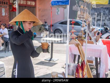 Februar 25 2023 - George Town - Penang - Malaysia - wunderschöne junge Frau aus Malaysia mit einem speziellen Hut und schwarz gekleidet verkauft Kaffee an Touristen smi Stockfoto