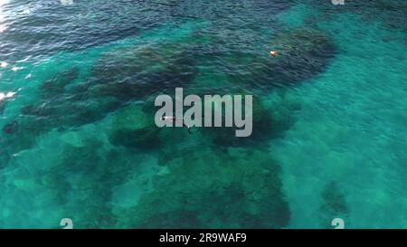 Albisola, Italien - 13. Juni 2021: Taucher schwimmt und taucht in der Nähe der Küste des ligurischen Meeres in transparentem, flachem, türkisfarbenem Wasser. Draufsicht oben Stockfoto