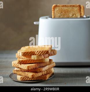 Ein Stapel getoasteter Brotscheiben und ein Toaster mit Unschärfe-Effekt auf dem Küchentisch Stockfoto