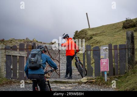 Zwei Männer fahren mit dem Mountainbike den Llanberis Path hinauf zum Gipfel des Snowdon (Yr Wyddfa) in Snowdonia, Wales im Februar. Stockfoto