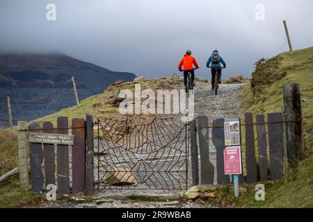 Zwei Männer fahren mit dem Mountainbike den Llanberis Path hinauf zum Gipfel des Snowdon (Yr Wyddfa) in Snowdonia, Wales im Februar. Stockfoto