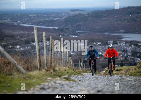 Zwei Männer fahren mit dem Mountainbike den Llanberis Path hinauf zum Gipfel des Snowdon (Yr Wyddfa) in Snowdonia, Wales im Februar. Stockfoto