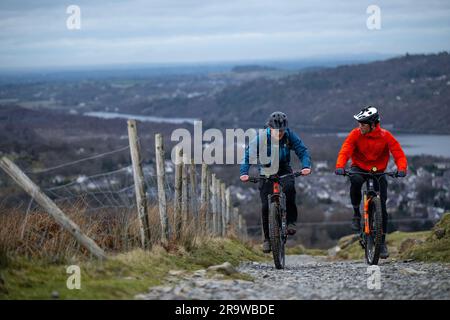 Zwei Männer fahren mit dem Mountainbike den Llanberis Path hinauf zum Gipfel des Snowdon (Yr Wyddfa) in Snowdonia, Wales im Februar. Stockfoto