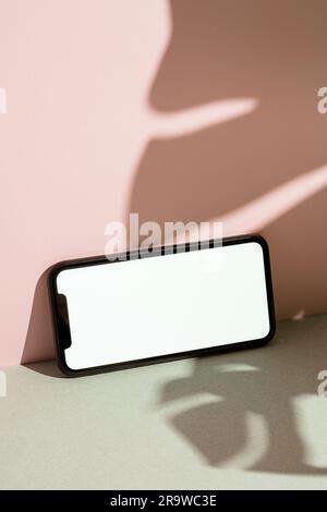 Weißes Smartphone-Modell, Vorlage auf pinkfarbenem und grauem Hintergrund mit montera-Blattschatten Stockfoto