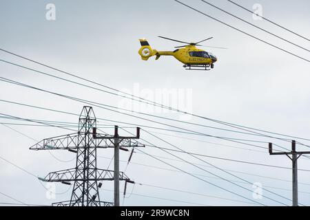 Gelber Airbus Helicopter in der Nähe von Hochleistungs-Pylonlinien Stockfoto