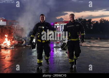 Das Team der tapferen Feuerwehrleute geht zur Kamera. Im Hintergrund Sanitäter und Feuerwehr Rettungsteam bekämpfen Feuer in Autounfall, Versicherung und Rettung von Menschen Stockfoto