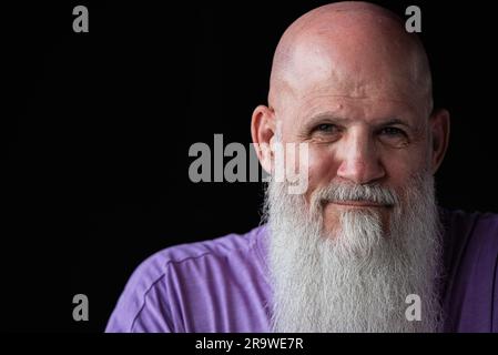 Porträt eines Mannes mit langem grauem Bart, der ein lilafarbenes T-Shirt im Nahaufnahme-Porträt trägt Stockfoto