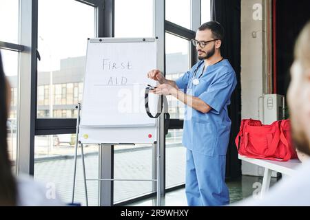 Sanitäter in Brille und blauer Uniform, steht auf dem Flipchart mit erste-Hilfe-Schriftzug und zeigt den Schülern Druckstaub auf verschwommen für Stockfoto