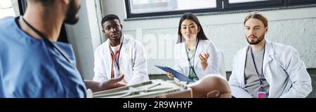 Junge asiatische Frau, die während eines erste-Hilfe-Seminars mit interrassistischen Studenten eine Frage an einen medizinischen Lehrer mit HLW-Übungspuppe stellt, anwerben und praktizieren Stockfoto