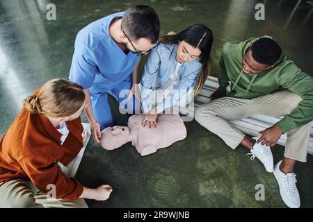 Erste-Hilfe-Seminar, kardiopulmonales Reanimationstraining, Hochwinkel-Blick auf junge asiatische Frau, die Thoraxkompressionen auf HLW-Übungspuppe in der Nähe von Medical i Stockfoto