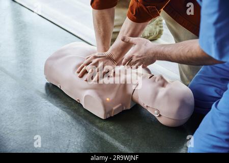 Erste-Hilfe-Trainingsseminar, Teilansicht des medizinischen Lehrers, der mit der Hand zeigt und dem helfenden Mann, der Thoraxkompressionen an der HLW-Prüfpuppe, Life-savi macht Stockfoto