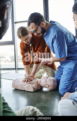 Erste-Hilfe-Trainingsseminar, professioneller Sanitäter, der jungen Mann hilft, Thoraxkompressionen an der HLW-Übungspuppe in der Nähe multiethnischer Teilnehmer durchzuführen, effektiv Stockfoto