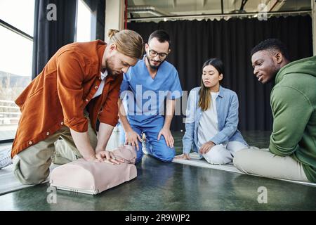 Ein junges multiethnisches Team und ein professioneller Sanitäter, der einen afroamerikanischen Mann beobachtet, der während der ersten Hilfe-Übung Thoraxkompressionen an der HLW-Prüfpuppe durchführt Stockfoto