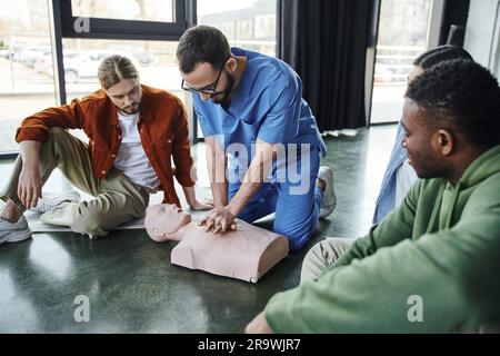 Professionelles medizinisches Fachpersonal, das Thoraxkompressionen an der HLW-Prüfpuppe durchführt und die kardiopulmonale Reanimation jungen multiethnischen Teilnehmern von zeigt Stockfoto