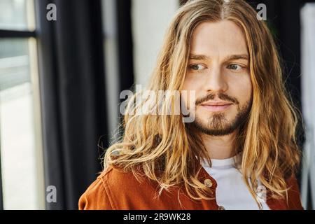 Porträt eines nachdenklichen, langhaarigen und bärtigen Geschäftsmanns, der in einem modernen Büro wegsieht, Individualität und Selbstvertrauen, Hipster-Stil, trendige Casu Stockfoto