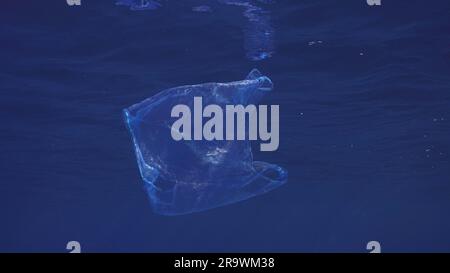 Blauer Einweg-Plastikbeutel schwimmt unter der Oberfläche in blauem Wasser. Plastiktüte, die ins Meer geworfen wurde, treibt morgens unter blauem Wasser, Rot Stockfoto