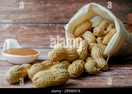 Geschälte Erdnüsse in einem Stoffbeutel und Löffel mit Erdnussbutter auf einem Holztisch Stockfoto