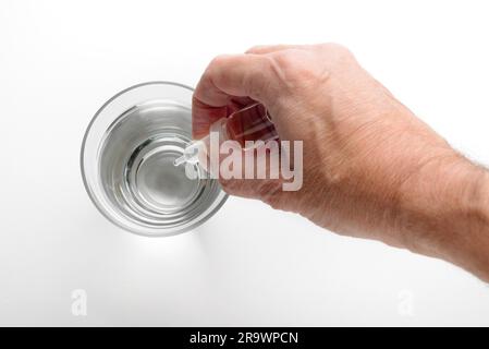 Die Hand des Menschen setzen Apotheke Tropfen in ein Glas transparent Wasser auf weißem Hintergrund Stockfoto