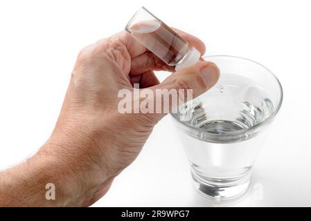 Die Hand des Menschen setzen Apotheke Tropfen in ein Glas transparent Wasser auf weißem Hintergrund Stockfoto