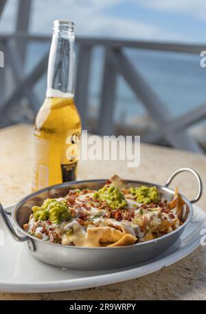 Ein Teller mit unwiderstehlichen Nachos mit geschmolzenem Käse, serviert auf einem kühlen Marmortisch im Freien, begleitet von einem eiskalten Bier Stockfoto