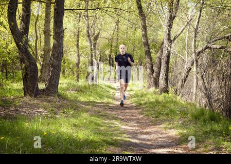 Ein senior Mann in Schwarz getragen läuft im Wald in einem warmen Frühlingstag Stockfoto