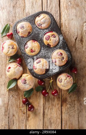 Hausgemachte Kirsch-Muffins in Cupcake-Einlagen und frische Kirschen im Hintergrund. Vertikale Draufsicht von oben Stockfoto
