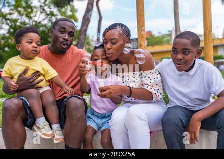 Afrikanische schwarze ethnische Familie mit Kindern auf dem Spielplatz, die Seifenblasen blasen Stockfoto