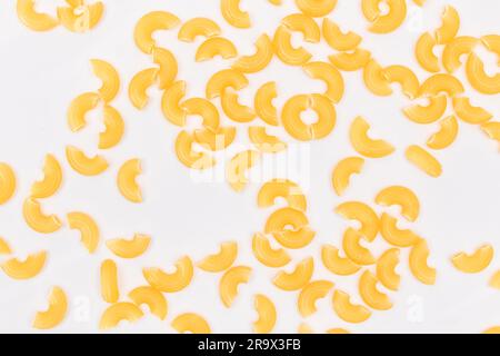 Verstreute ungekochte Chifferi Rigati Pasta auf weißem Hintergrund. Fett und ungesunde Lebensmittel. Klassische Trockene Makkaroni-Textur. Italienische Kultur und Küche. Rohe Pasta Stockfoto