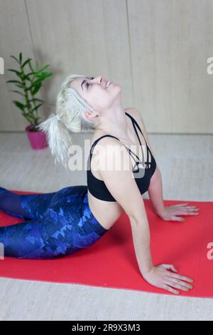 Junge Frau, die High-Cobra-Asana im Yoga-Studio praktiziert. Bhujangasana-Pose Stockfoto
