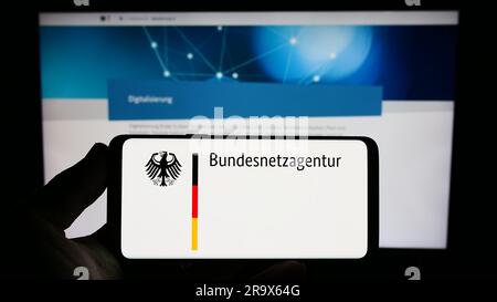 Person, die ein Smartphone mit dem Logo der Bundesnetzagentur (BNetzA) auf dem Bildschirm vor der Website hält. Konzentrieren Sie sich auf das Display des Telefons. Stockfoto