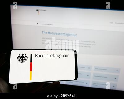 Person, die ein Mobiltelefon mit dem Logo der Bundesnetzagentur (BNetzA) auf dem Bildschirm vor der Webseite hält. Konzentrieren Sie sich auf das Display des Telefons. Stockfoto