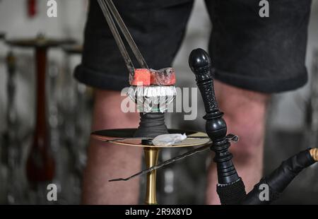 Sindelfingen, Deutschland. 29. Juni 2023. Ein Stück Kohle zum Erhitzen des Tabaks wird auf eine Wasserpfeife in einer Wasserpfeife gelegt. Shisha-Bars dominieren in vielen Städten zunehmend das Stadtbild. Aber der Whookah-Markt leidet unter zu vielen Regeln und Bürokratie, kritisieren die jungen Liberalen in Baden-Württemberg. (Zu dpa "Junge Liberale kritisieren Bürokratie für Hookah Bars") Kredit: Bernd Weißbrod/dpa/Alamy Live News Stockfoto