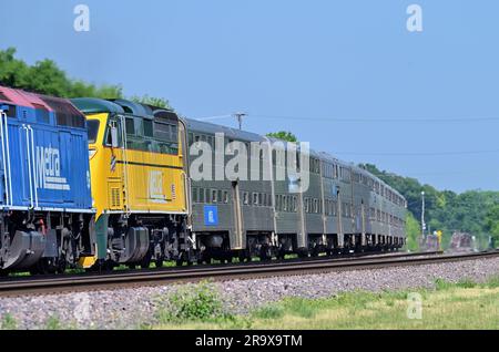 West Chicago, Illinois, USA. Ein Metra-Pendlerzug, der von zwei Lokomotiven geschoben wird, einschließlich einer speziell lackierten Einheit. Stockfoto