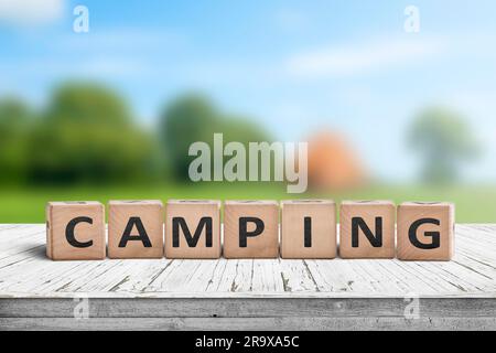 Camping-Wort auf einem Holzwürfelschild mit verschwommenem Hintergrund eines Campingplatzes im Sommer Stockfoto