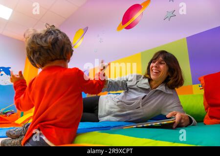 Lehrerin, die mit einem Buch spielt, Inneneinrichtung eines Kindergartens Stockfoto