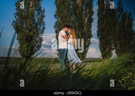 Seitenblick auf ein liebevolles Paar, das sich umarmt und anschaut, während es abends auf einer Wiese steht Stockfoto