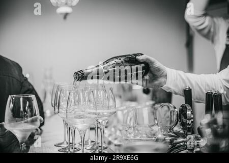 Eine Graustufenaufnahme eines Kellners, der Champagner in die Gläser gießt Stockfoto