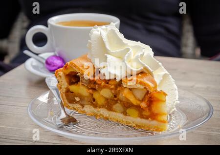 Apfelkuchen mit Schlagsahne auf der Terrasse sowie eine Tasse Kaffee mit einem lila osterei Stockfoto