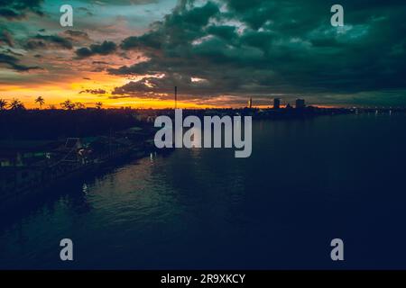 Panorama-Stadtbild bei Sonnenuntergang mit großem Fluss im Vordergrund und strommwolken im Hintergrund in Thailand. Stockfoto