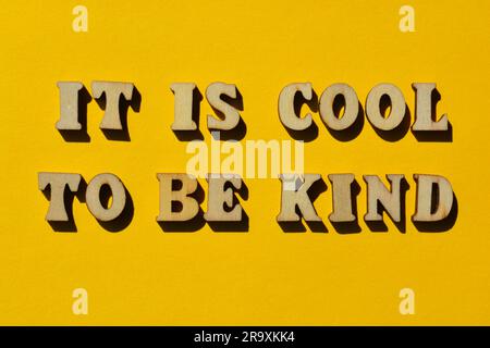 Es ist cool, nett zu sein, Wörter in hölzernen Buchstaben isoliert auf hellem gelbem Hintergrund als Bannerüberschrift Stockfoto