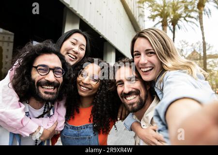 Vielfältige Gruppe von Freunden, die lachen, sich umarmen und ein Selfie auf der Straße machen. Fröhliche multiethnische Gruppe von jungen Hipstern, die ein Foto machen Stockfoto