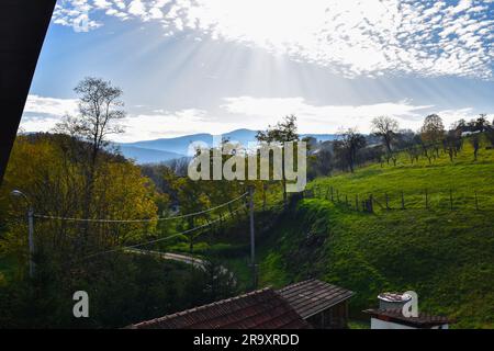 Ein hügeliges Dorf, eine gemähte steile Wiese und eine Straße, die sich durch das Dorf schlängelt Stockfoto