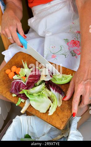 Detail einer weiblichen Hand Entsorgung der organischen Abfälle in einem geeigneten Behälter mit Küche im Hintergrund Stockfoto