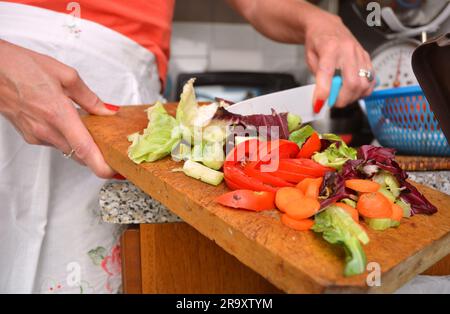 Detail einer weiblichen Hand Entsorgung der organischen Abfälle in einem geeigneten Behälter mit Küche im Hintergrund Stockfoto